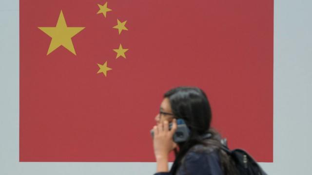 西班牙马德里2019年联合国气候变化大会中国展馆内一位女子讲着手机走过一面中国国旗（3/12/2019）