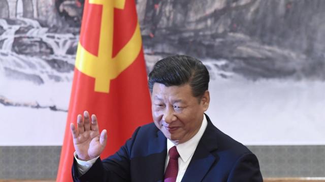 Xi Jinping saluda con una bandera comunista de fondo.