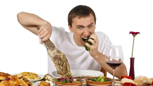 Мужчина за столом с бараньей ногой в руке