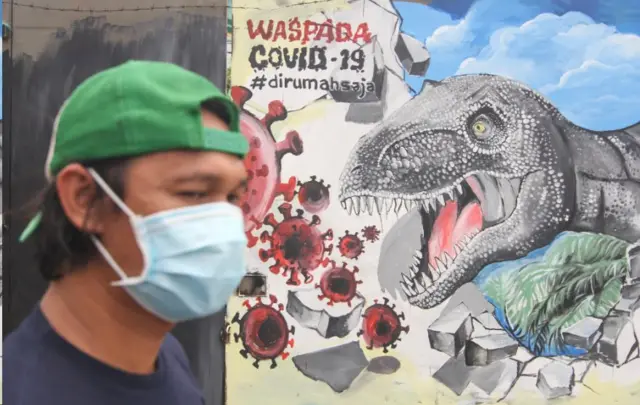 Seorang warga melintas di depan mural bertema COVID-19 di Jalan Baru, Depok, Jawa Barat, Senin (30/3/2020)