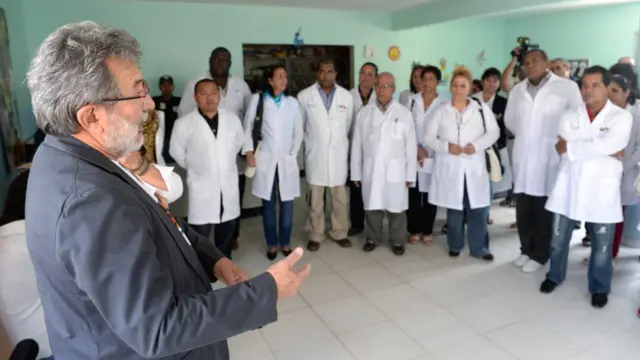 Alguns médicos participantes do Mais Médicos fazem roda enquanto escutam um homem engravatado falar