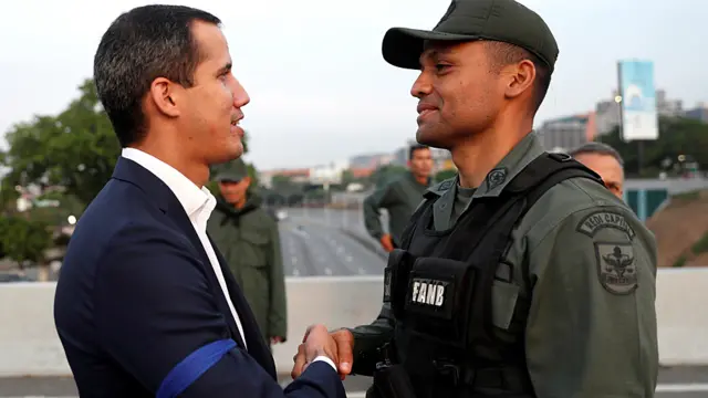 Juan Guaidó, com uma fita azul no braço, aperta a mãobanca baixa no aviatorum militar