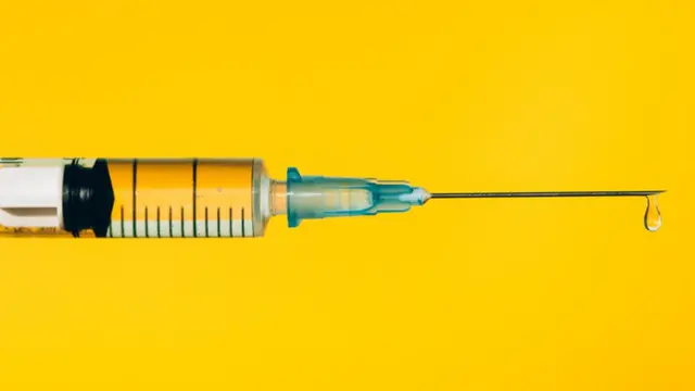 Foto de uma seringa de vacina num fundo amarelo