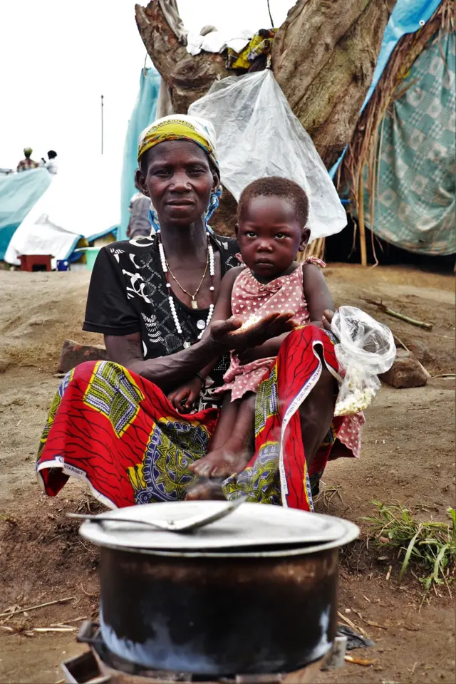 Une mère avec son fils dans les bras qui fait la cuisson.