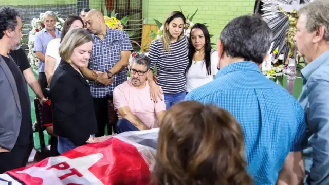 Gleisi Hoffmann e outras pessoas com feições consternadas em volta de caixão, que é coberto por bandeira do PT