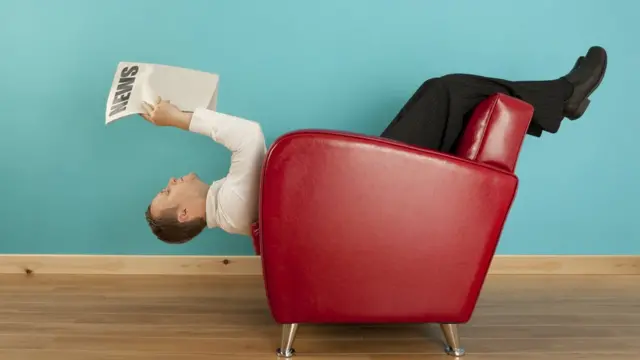 Hombre lee el diario en una posición extraña.