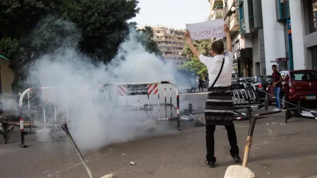 Umwe mu biyamiriza leta ateruye icapa iruhande y'ahatewe imyuka irakira mu muji wa Cairo 25/04/2016.