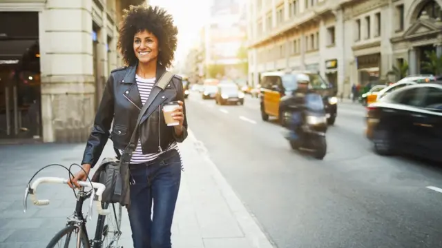 Девушка идет по городу с кофе и велосипедом