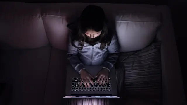 Niña con computadora en la oscuridad.