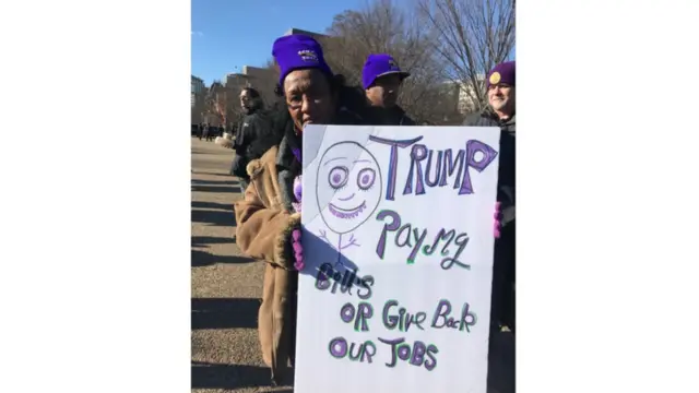 穆罕默德在白宫前举起手上的标语，上面写道："特朗普，付我的账单，或者还我们工作。"