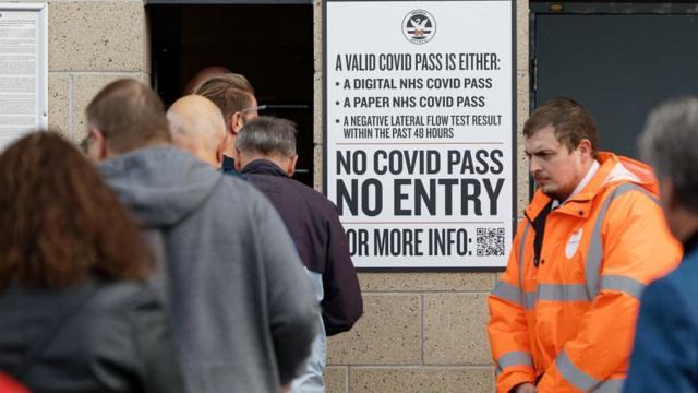 people queue into football stadium by sign reading 'no covid pass, no entry'