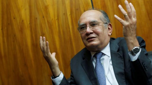 Gilmar Mendes gesticula com as mãos para cima e sorri timidamente