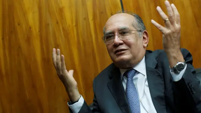 Gilmar Mendes gesticula com as mãos para cima e sorri timidamente