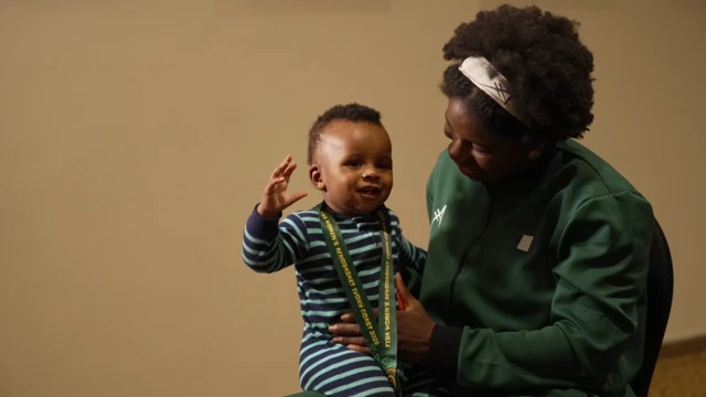 Baby Bently wear im mother 2025 AfroBasket Gold medal for neck wit smile for im face, im also raise in hand as im mama dey play wit am. 