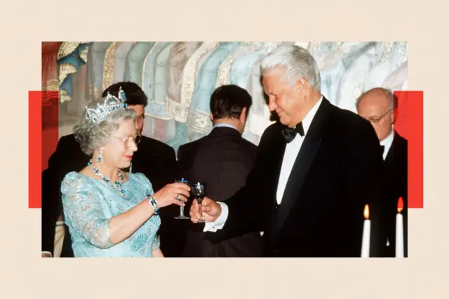 Nữ hoàng Elizabeth II, trong bộ váy màu xanh nhạt và đội vương miện, nâng ly chúc mừng ông Boris Yeltsin (bên phải), người đang mặc lễ phục.