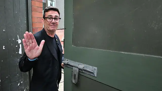 Ubrany w czarny garnitur i koszulkę Andy Burnham macha na pożegnanie, opuszczając Muzeum Historii Ludowej w Manchesterze. 29 czerwca 2026 roku.
