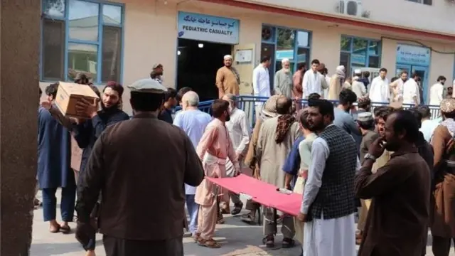 Dos hombres llevan una camilla, mientras una multitud de afganos se congregan frente a la entrada de un hospital en la provincia de Nangarhar, Afganistán.