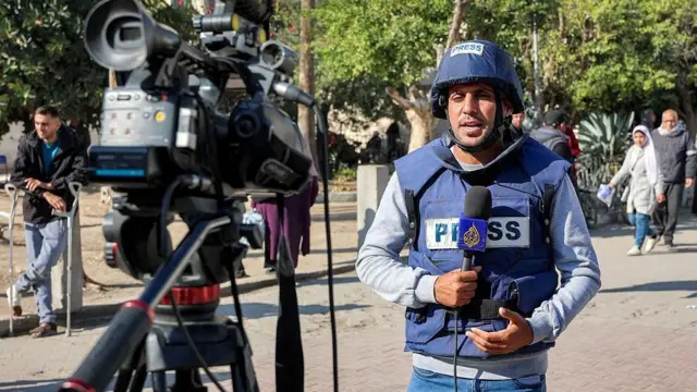 الصحفي محمد قريقع يمسك مايكروفون قناة الجزيرة أمام كاميرا