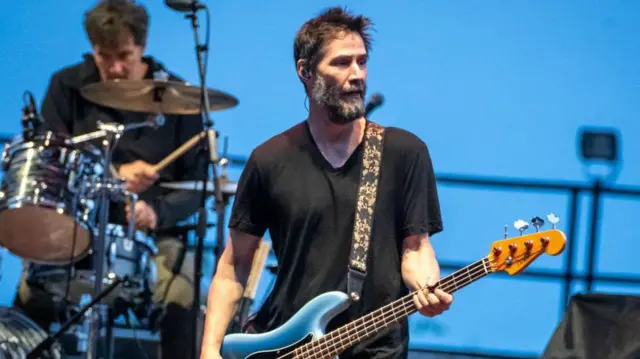 Keanu Reeversaposte na copa do mundocamiseta preta aparece tocando guitarraaposte na copa do mundouma apresentação. Ao fundo, um baterista tocando bateria