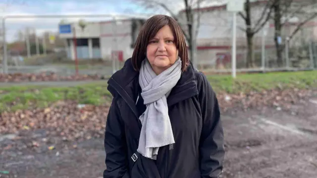 Tracy Ward, de Chellaston, Derby, comentó que este multicine les dio a los espectadores muchas más opciones. Aparece en la foto con un abrigo negro y una bufanda gris. El cine se ve borroso al fondo, rodeado por una valla.