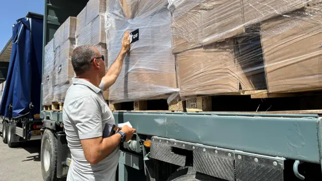 یو سړی د غزې بشري مرستو بنسټ لوګو سره سټیکر ضمیمه کوي، ترڅو غزې ته د ننوتلو په تمه په یوه لارۍ کې مرسته وکړي.