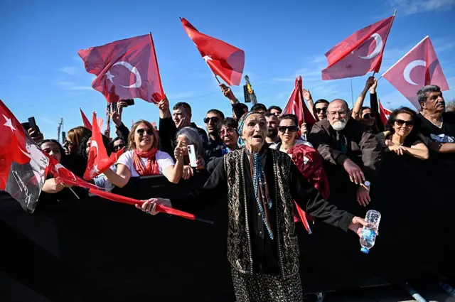 İmamoğlu'nun tutuklanmasıyla beraber başlayan protestolara katılan bir kalabalık. En önde yaşlı bir kadın Türkiye bayrağı sallıyor