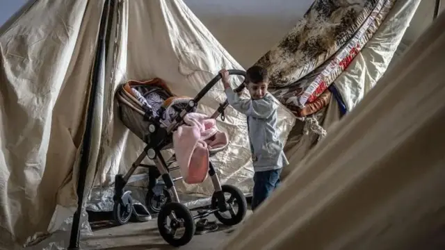 پسری آواره، کالسکه‌ای را به داخل چادر خانواده‌اش در اردوگاه موقت در استادیوم بیروت هل می‌دهد
