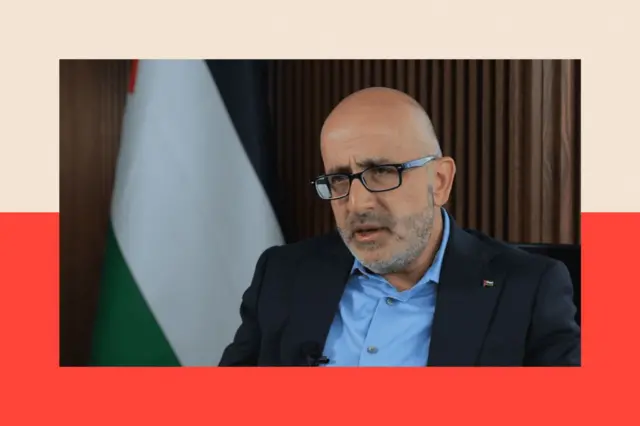  وزير التخطيط في السلطة الفلسطينية استيفان سلامة جالساً وخلفه العلم الفلسطيني.