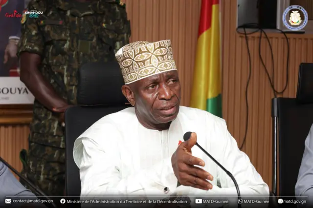 Ibrahima Kalil Condé de l'Administration du territoire et de la Décentralisation en boubou blanc, parle dans un micro.