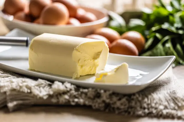 Bir masanın üzerinde bir tabak içinde tereyağı bulunuyor. Arkada masanın üzerinde ve bir tabağın içinde çok sayıda yumurta var. 