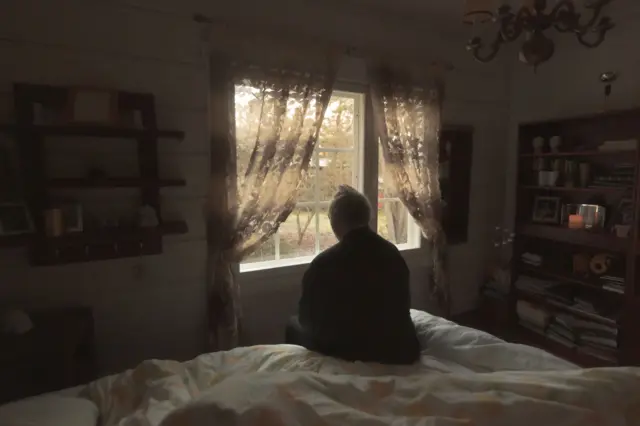 persona sentada en una cama mirando a la ventana