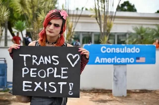 Persona trans con un cartel en la mano donde se lee 