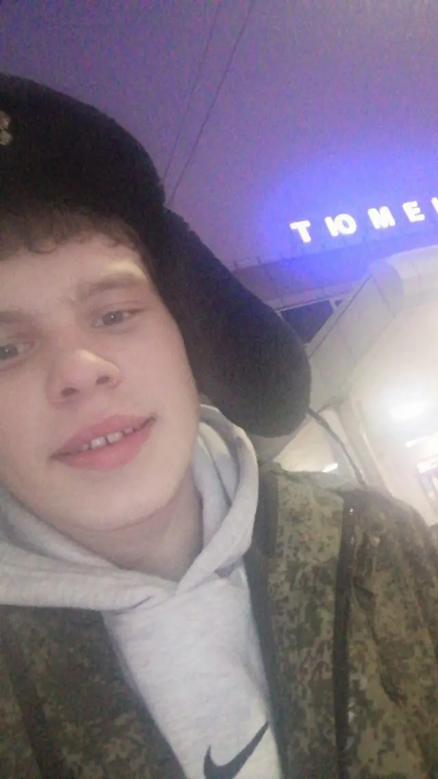 Vitaly Ivanov e uma foto em que usa um chapéu preto e um moletom cinza por baixo de um casaco. Ele está sorrindo.