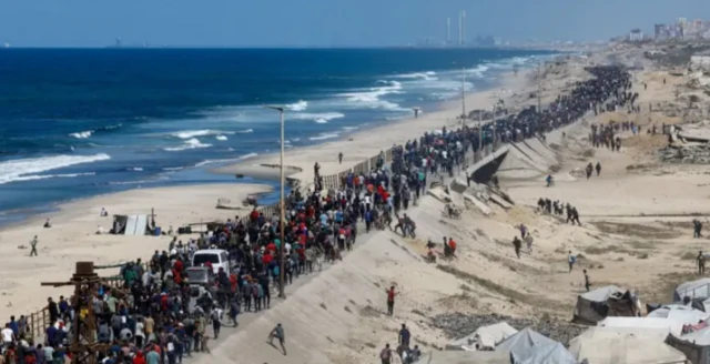 Centenas de pessoas caminham ao longo de uma estrada costeira, na tentativa de chegar ao norte da Faixa de Faza