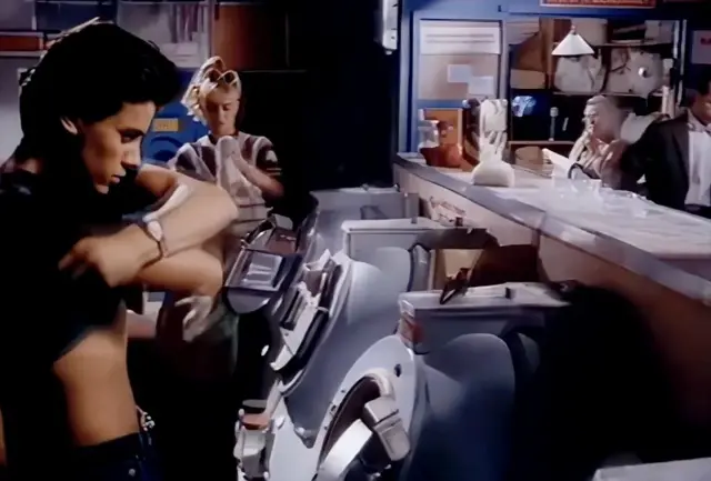 세탁기 앞에서 상의를 벗는 닉 케이먼과 그의 주변에 있는 여성들