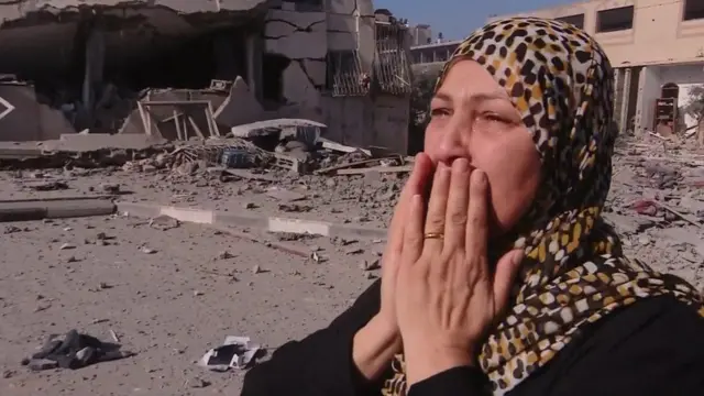 A woman holds her face and cries amid destroyed buildings