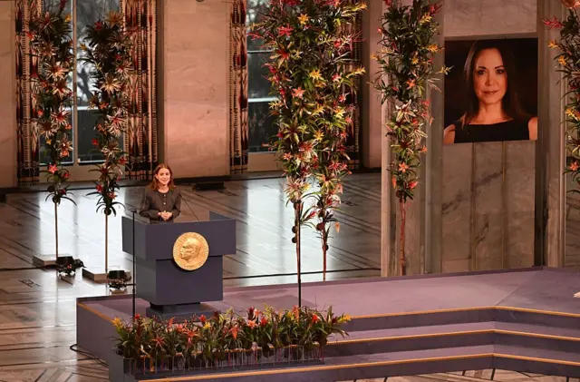 Imagem mostra filha de María Corina no palco e uma foto da mãe ao fundo