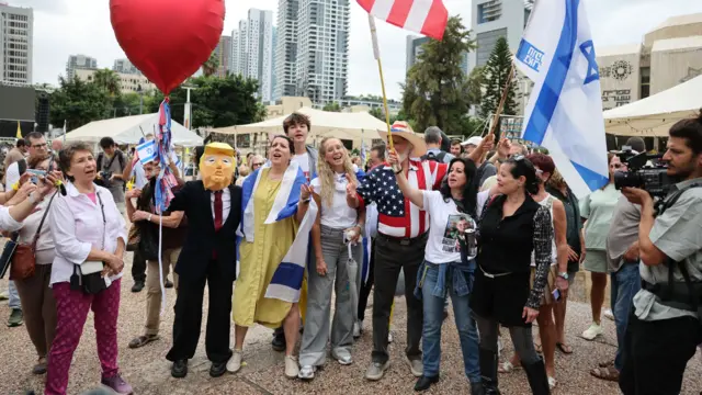 Люди с флагами Израиля и США празднуют после объявления мирного соглашения на площади Заложников в Тель-Авиве, один мужчина одет в костюм ковбоя, другой изображает Дональда Трампа.