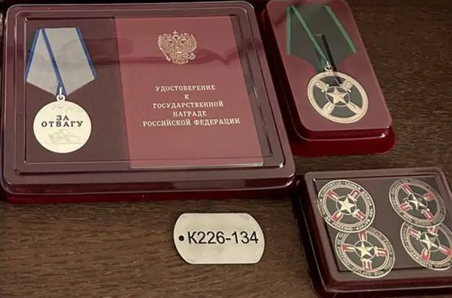 Uma placaglobalvip apostasidentificação com a inscrição 'K226-134', ao ladoglobalvip apostasuma medalha gravada com as palavras 'por bravura'