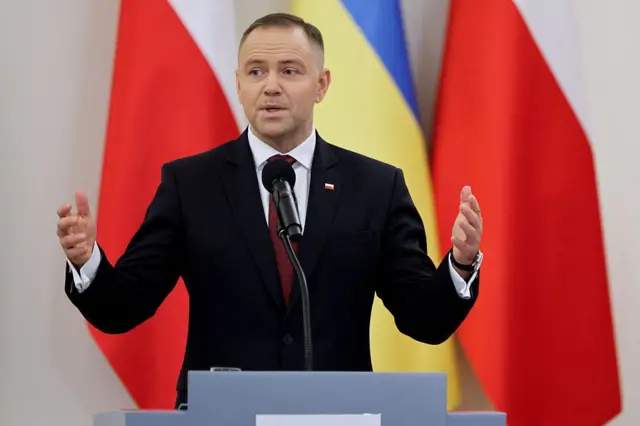 Навроцкий произносит речь за трибуной, жестикулируя обеими руками. На фоне — флаги Польши и Украины.