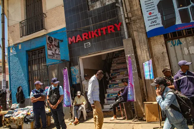 Beaucoup de gens dans la rue par une chaude journée ensoleillée. Les gens vendent de la nourriture, des articles ménagers ou vaquent à leurs occupations. Architecture d'Antananarivo.