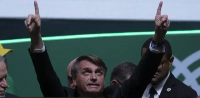 Bolsonaro aparece em evento de terno, olhando para o céu e levantando os dedos para cima