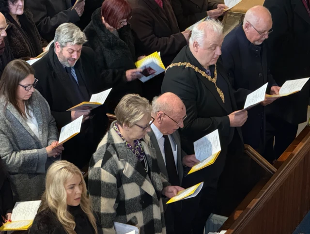 Parte de tres bancos que incluyen personas sosteniendo el orden del servicio.