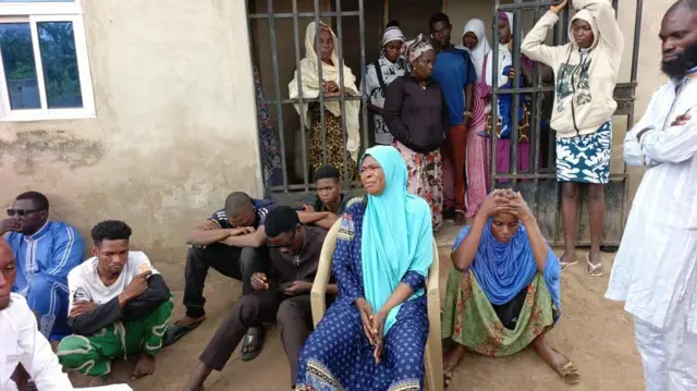 Aworan bi Iya Sanku ṣe n sunkun ati bi awọn abanikẹdun ṣe yi i ka. Awọn kan jokoo silẹẹ, awọn kan si duro mọ irin ninu ile.