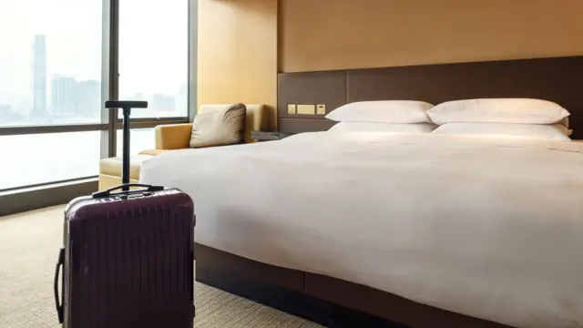 设计图片：香港某酒店房间内的睡床，行李箱停放在旁，左侧窗户能看见维多利亚港景色