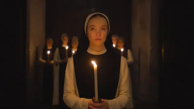 A atriz Sydney Sweeney vestida como freira e segurando uma vela, em imagem do filme Imaculada 