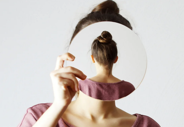 Mulher olhando para espelho, que mostra seu reflexo de costas