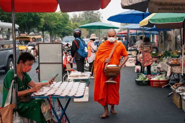 ชาวเชียงใหม่ต้องใช้ชีวิตกลางหมอกควันฝุ่น PM2.5 ที่ปกคลุมทั่วเมืองเมื่อ 3 เม.ย. ทั้งพระสงฆ์ที่ออกบิณฑบาต แม่ค้า ประชาชนที่ออกไปจับจ่ายที่ตลาดประตูเชียงใหม่ต้องสวมหน้ากากป้องกันฝุ่น