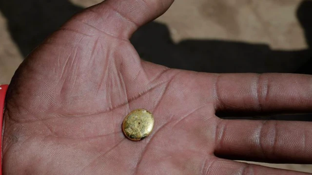 Elinde küçük bir altın tutan bir el kameraya bu altını gösteriyor
