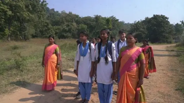 রাস্তার মাঝখান দিয়ে হাঁটছে গ্রামের কয়েকজন শিক্ষার্থী, তাদের ঘিরে আছেন চারজন নারী